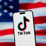 The TikTok app and logo are seen on a mobile device in front of a US flag